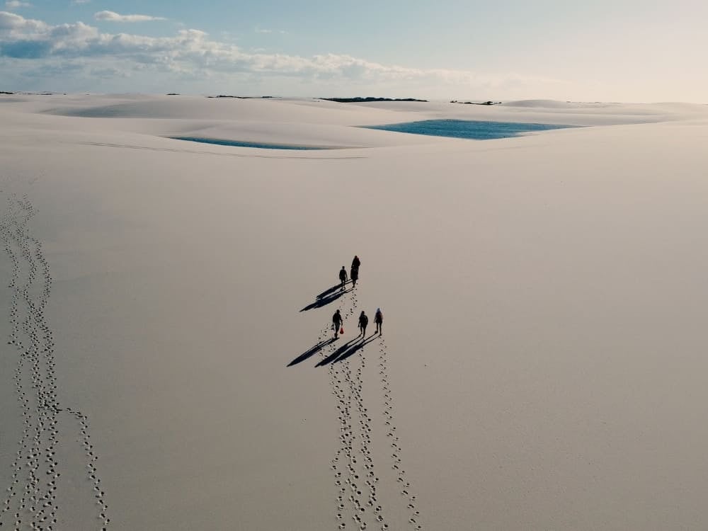 Veduta aerea di un gruppo in trekking sulle immense dune di sabbia bianca dei Lençóis Maranhenses, con piccole lagune azzurre sullo sfondo. Veduta aerea di un gruppo in trekking sulle immense dune di sabbia bianca dei Lençóis Maranhenses, con piccole lagune azzurre sullo sfondo.