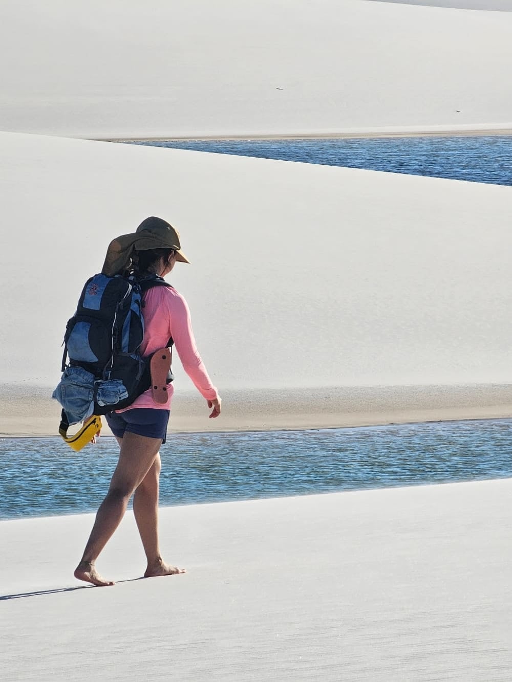 Un viaggiatore con lo zaino cammina scalzo sulle dune di sabbia bianca vicino a una laguna azzurra, durante un trekking impegnativo nei Lençóis Maranhenses. Un viaggiatore con lo zaino cammina scalzo sulle dune di sabbia bianca vicino a una laguna azzurra, durante un trekking impegnativo nei Lençóis Maranhenses.