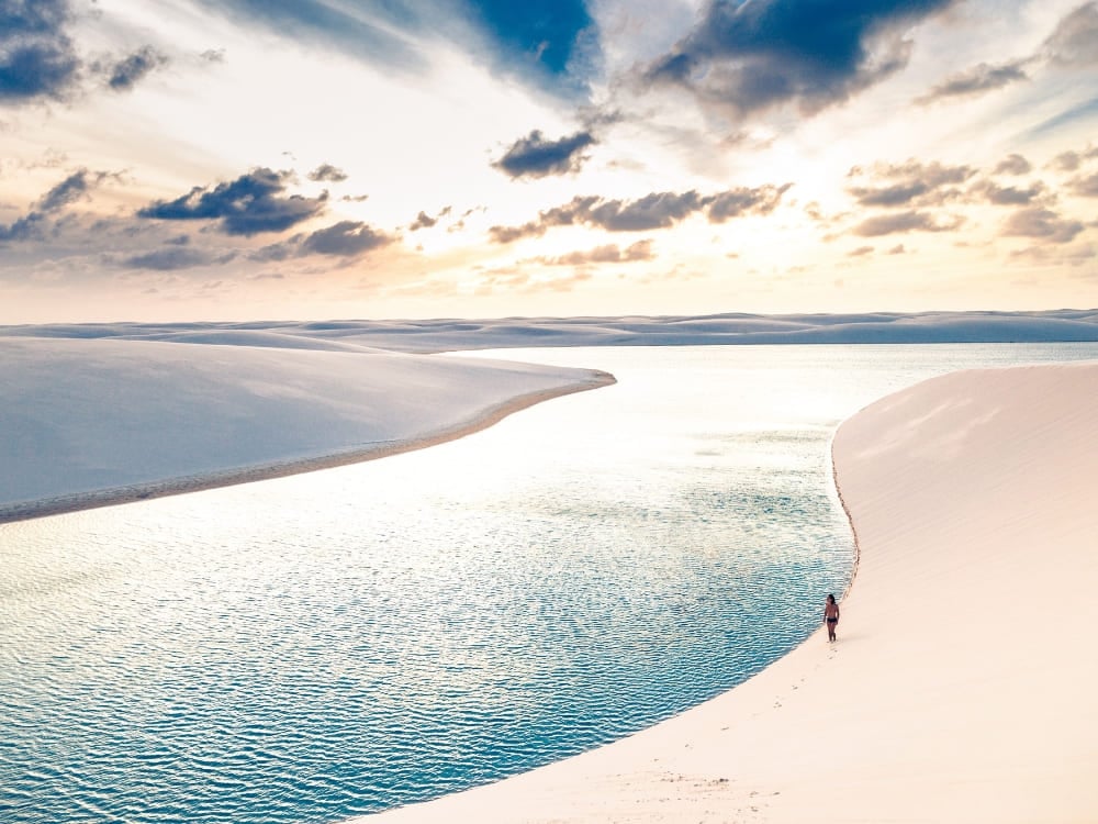 Un viaggiatore cammina sul bordo di una laguna azzurra e limpida circondata dalle dune di sabbia, nel periodo migliore per visitare i Lençóis Maranhenses. Un viaggiatore cammina sul bordo di una laguna azzurra e limpida circondata dalle dune di sabbia, nel periodo migliore per visitare i Lençóis Maranhenses.