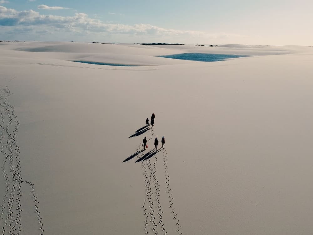 Un piccolo gruppo di escursionisti proietta ombre lunghe mentre attraversa una distesa immensa di dune di sabbia bianca, durante un trekking di più giorni nei Lençóis Maranhenses. Un piccolo gruppo di escursionisti proietta ombre lunghe mentre attraversa una distesa immensa di dune di sabbia bianca, durante un trekking di più giorni nei Lençóis Maranhenses.