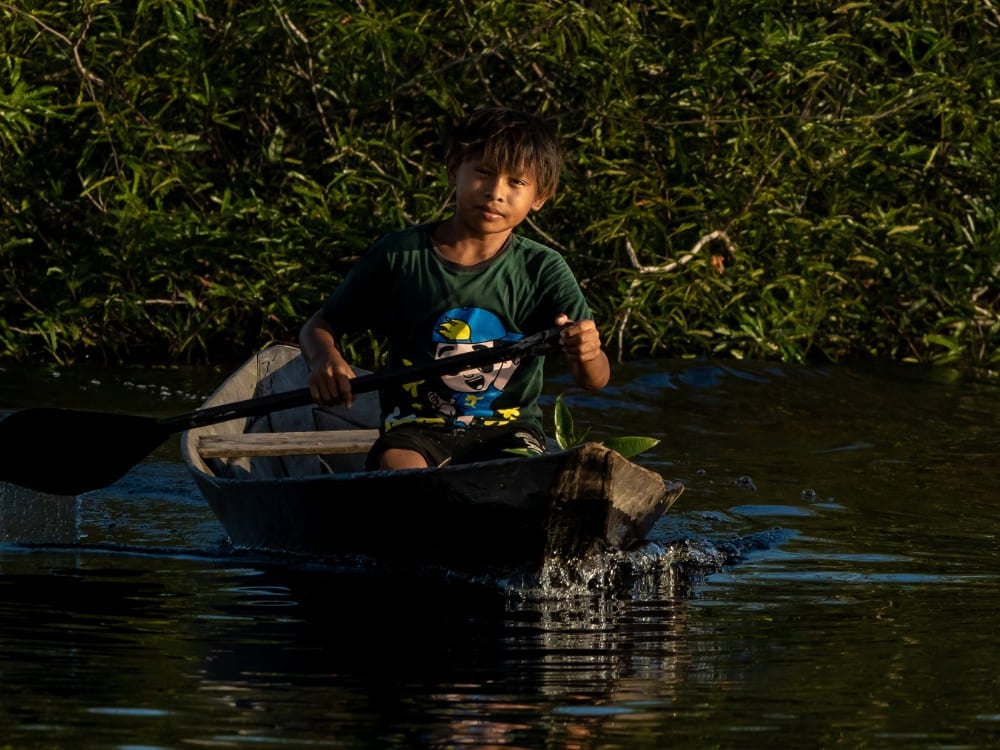 Un bambino che pagaia su una canoa di legno lungo un fiume scuro, immagine della vita quotidiana delle comunità rivierasche dell'Amazzonia. Un bambino che pagaia su una canoa di legno lungo un fiume scuro, immagine della vita quotidiana delle comunità rivierasche dell'Amazzonia.