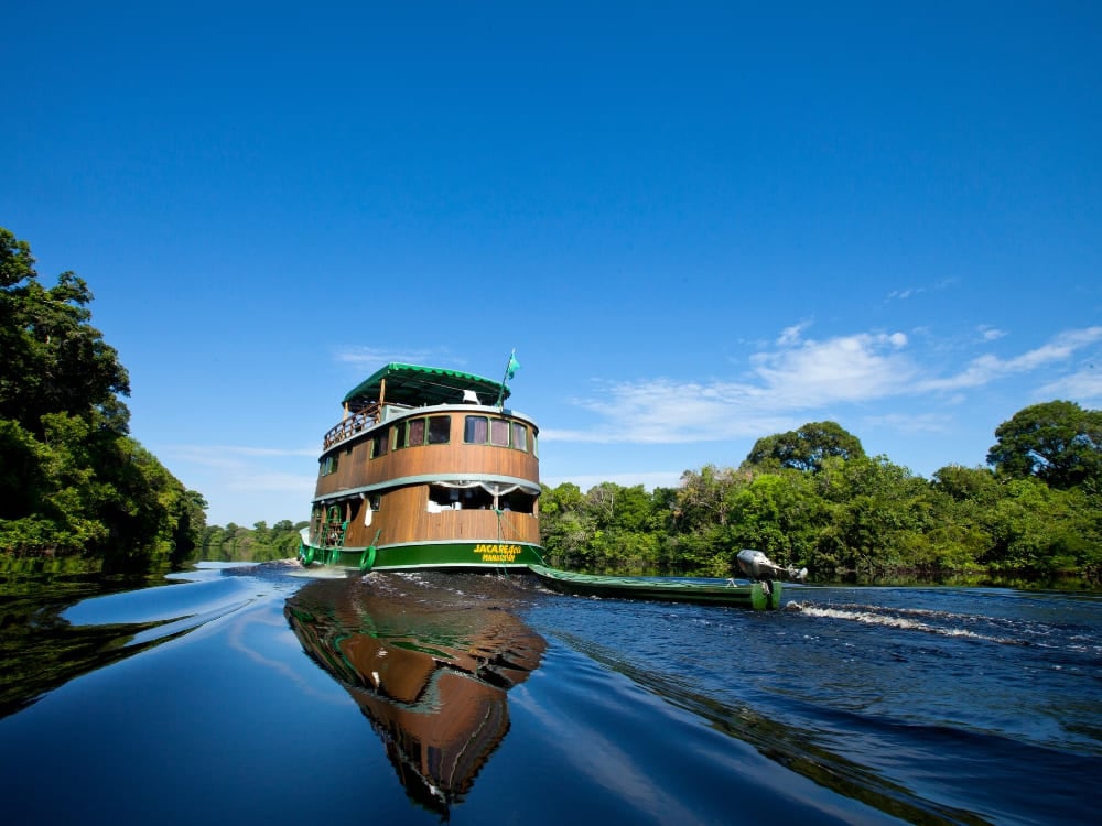 Un battello fluviale tradizionale in legno, a più ponti, naviga sulle acque scure e riflettenti dell'Amazzonia. Un battello fluviale tradizionale in legno, a più ponti, naviga sulle acque scure e riflettenti dell'Amazzonia.