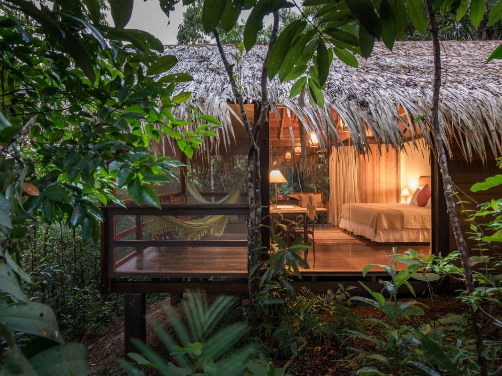 Un bungalow di lusso con tetto di paglia e luci calde all'interno, immerso tra gli alberi verdi dell'Anavilhanas Jungle Lodge. Un bungalow di lusso con tetto di paglia e luci calde all'interno, immerso tra gli alberi verdi dell'Anavilhanas Jungle Lodge.