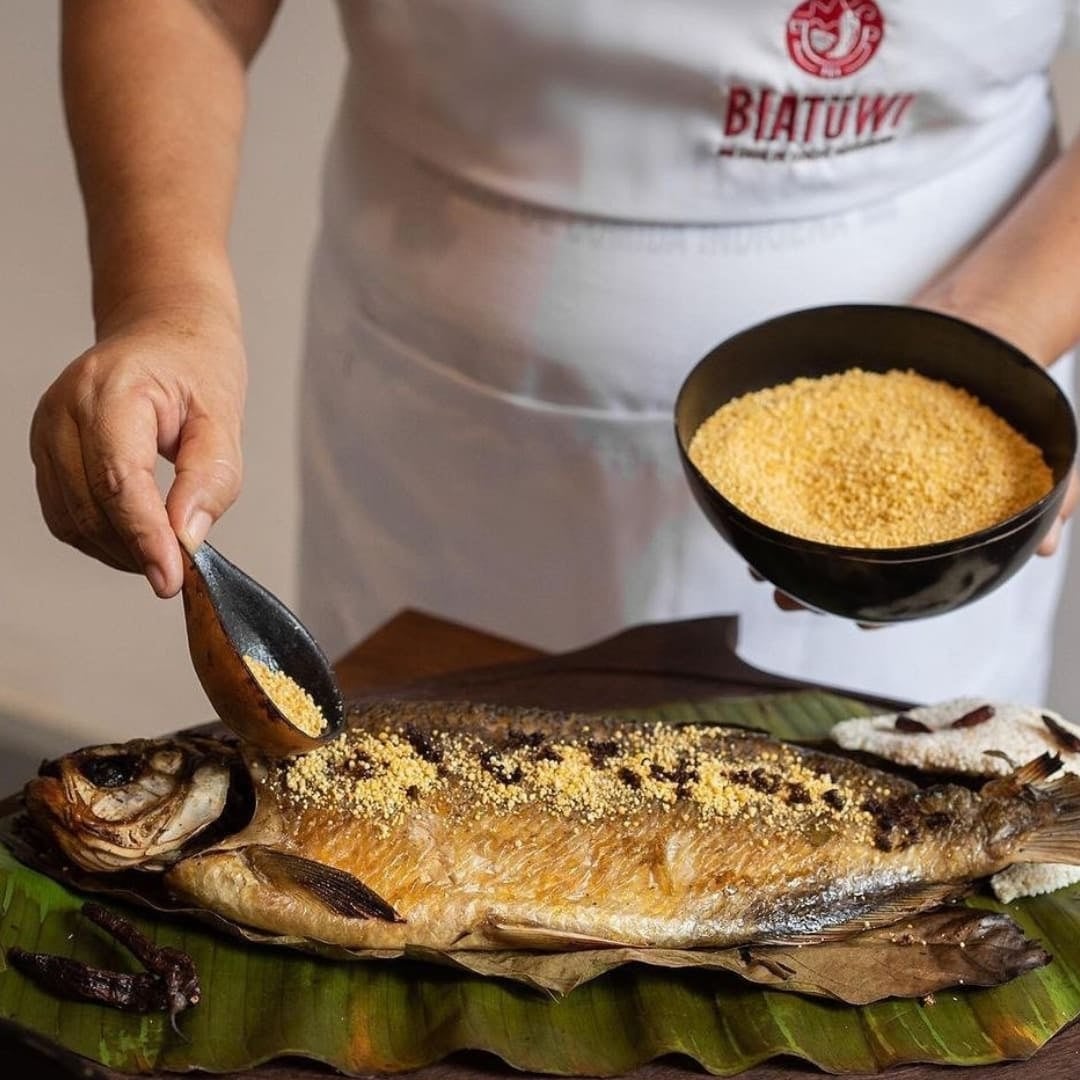 Primo piano di una persona che spolvera farina di manioca su un pesce arrosto servito su una foglia di banano. Primo piano di una persona che spolvera farina di manioca su un pesce arrosto servito su una foglia di banano.