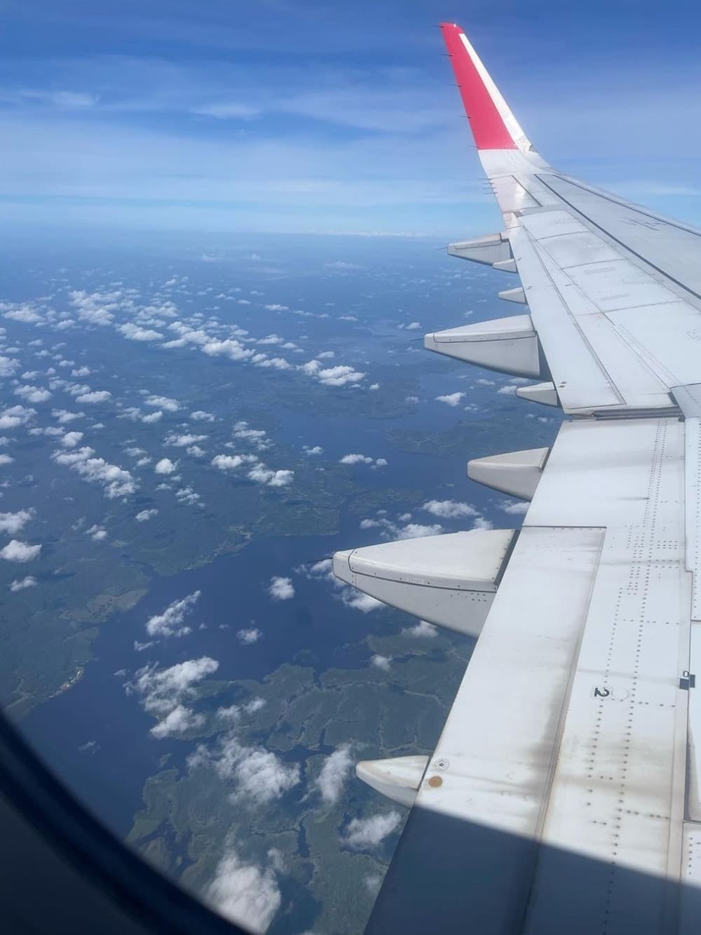 Vista dal finestrino di un aereo, oltre l'ala, verso le nuvole e il paesaggio amazzonico più in basso. Vista dal finestrino di un aereo, oltre l'ala, verso le nuvole e il paesaggio amazzonico più in basso.