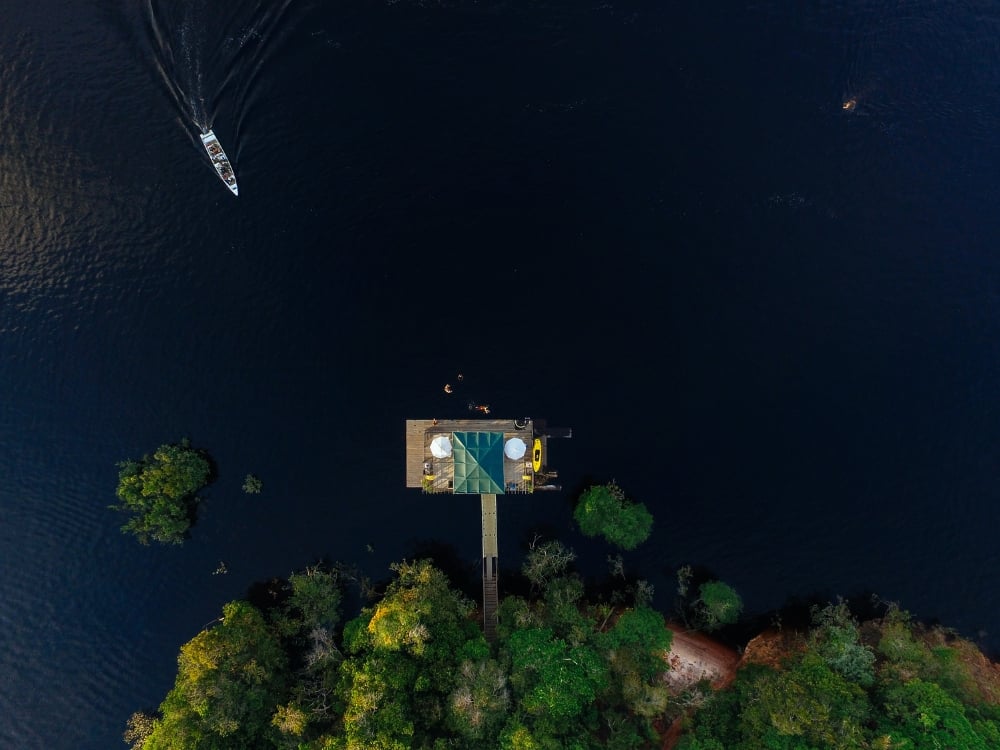 Ripresa aerea con drone di un eco-lodge su palafitte, circondato dalle acque scure del fiume amazzonico e dalla giungla rigogliosa. Ripresa aerea con drone di un eco-lodge su palafitte, circondato dalle acque scure del fiume amazzonico e dalla giungla rigogliosa.