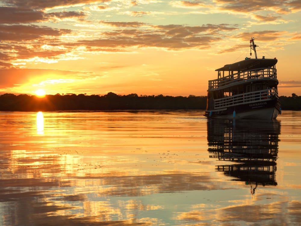 Tradizionale barca fluviale di legno naviga sulle acque calme dell'Amazzonia durante un tramonto dorato che si riflette sul fiume. Tradizionale barca fluviale di legno naviga sulle acque calme dell'Amazzonia durante un tramonto dorato che si riflette sul fiume.