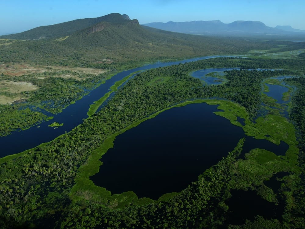 Veduta aerea di un fiume blu intenso che serpeggia tra le vaste pianure verdi della regione in cui si trova il Pantanal. Veduta aerea di un fiume blu intenso che serpeggia tra le vaste pianure verdi della regione in cui si trova il Pantanal.