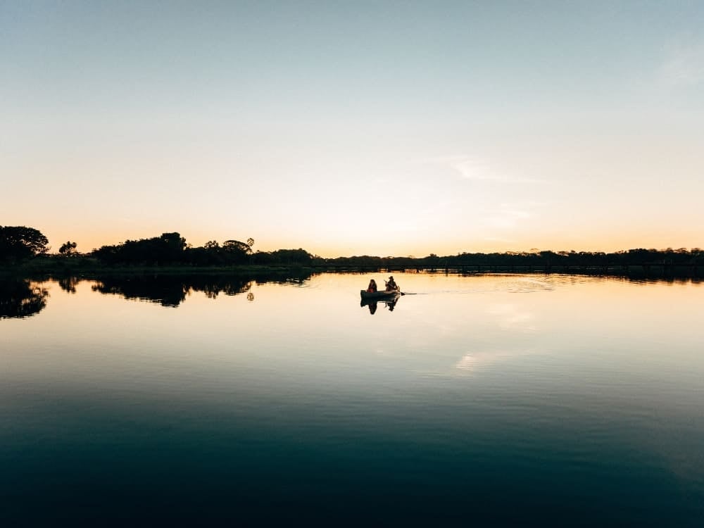 Due persone che pagaiano in canoa su un fiume calmo che riflette il cielo, nella zona in cui si trova il Pantanal. Due persone che pagaiano in canoa su un fiume calmo che riflette il cielo, nella zona in cui si trova il Pantanal.