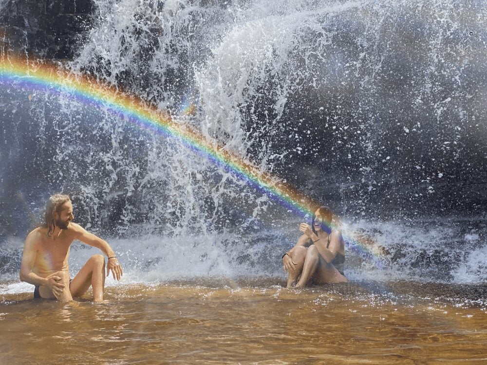 Two people relax in the warm waters at the base of a powerful waterfall with a bright rainbow in Chapada Diamantina. Two people relax in the warm waters at the base of a powerful waterfall with a bright rainbow in Chapada Diamantina.