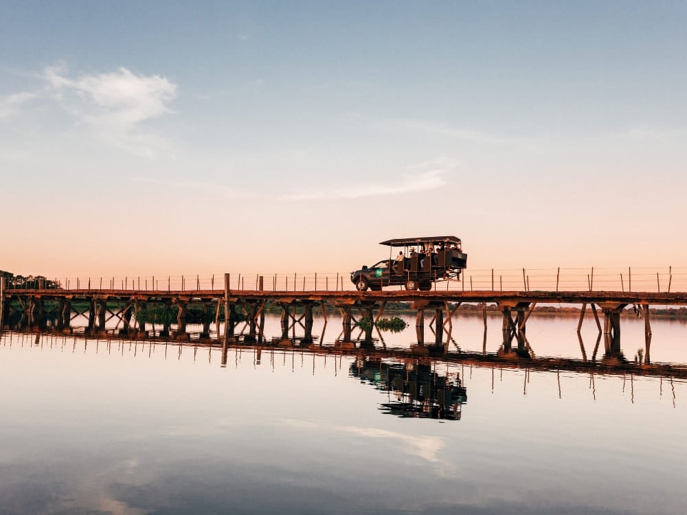 Un veicolo da safari attraversa un ponte di legno su un fiume che riflette il tramonto. Una scena tipica di un viaggio avventuroso e di un safari nel Pantanal. Un veicolo da safari attraversa un ponte di legno su un fiume che riflette il tramonto. Una scena tipica di un viaggio avventuroso e di un safari nel Pantanal.