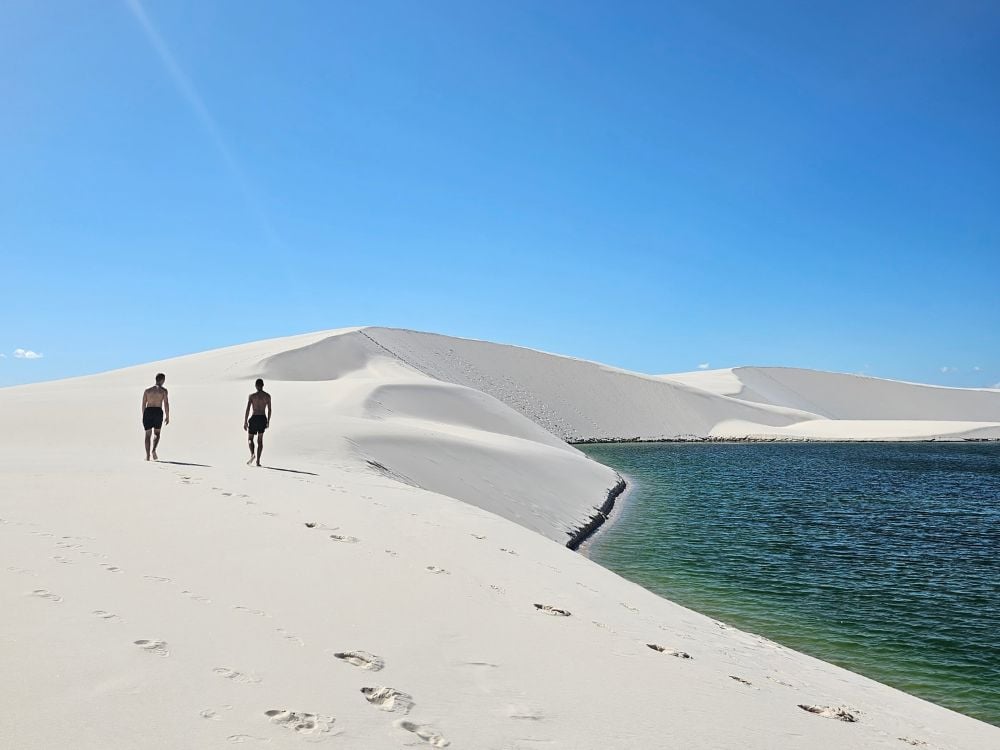 Un viaggiatore con lo zaino in spalla cammina sulle immense dune di sabbia bianca del Parco Nazionale dei Lençóis Maranhenses sotto un cielo nuvoloso. Un viaggiatore con lo zaino in spalla cammina sulle immense dune di sabbia bianca del Parco Nazionale dei Lençóis Maranhenses sotto un cielo nuvoloso.