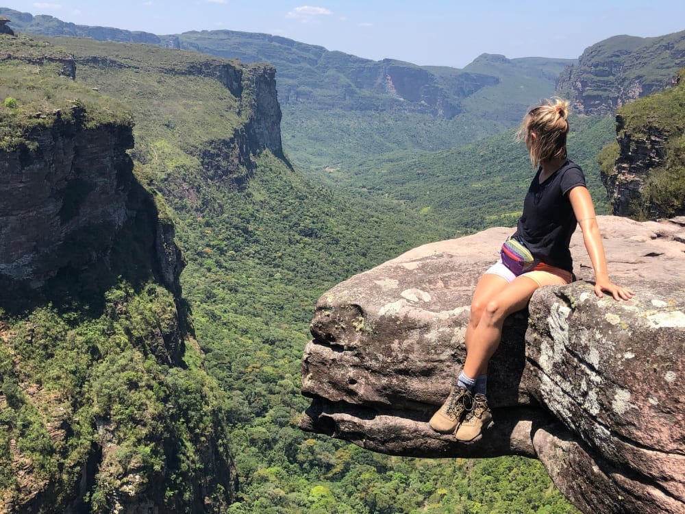 Escursionista seduta sul bordo di una parete rocciosa, con lo sguardo su un canyon verde e sugli altopiani in lontananza, durante un'avventura di ecoturismo. Escursionista seduta sul bordo di una parete rocciosa, con lo sguardo su un canyon verde e sugli altopiani in lontananza, durante un'avventura di ecoturismo.