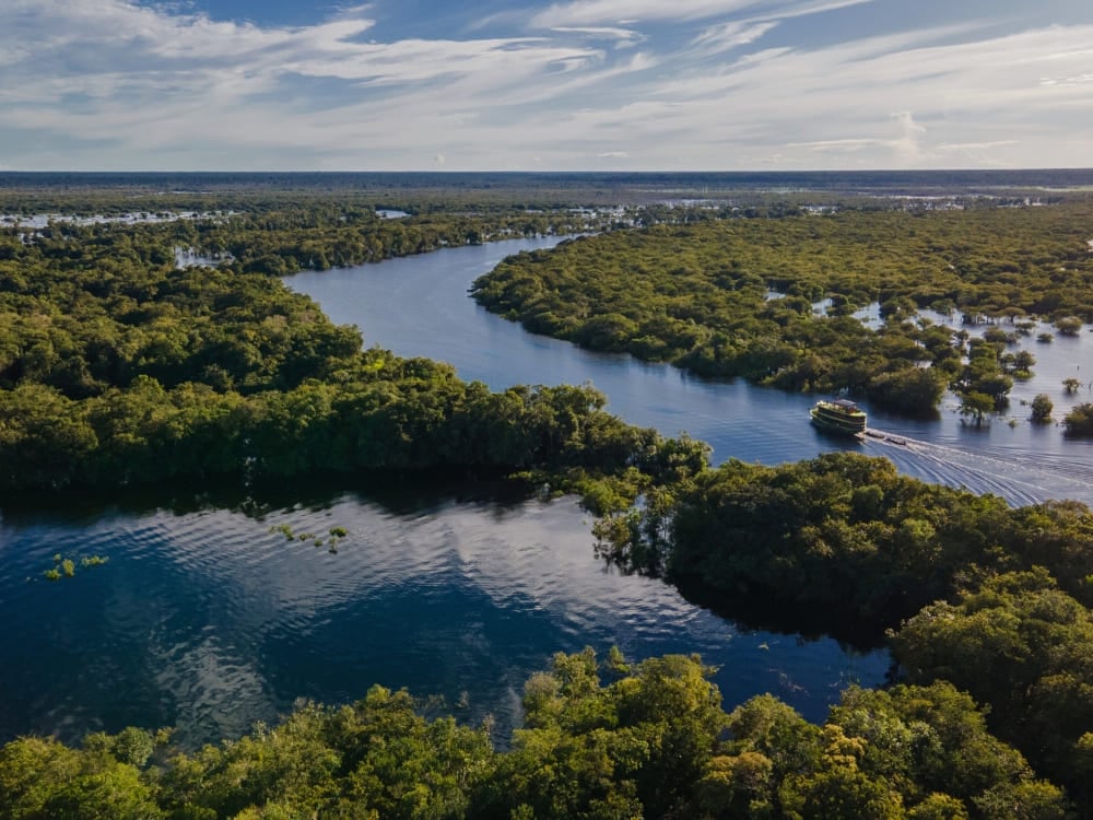 Barca fluviale in navigazione sul Rio delle Amazzoni, circondata dalla foresta Barca fluviale in navigazione sul Rio delle Amazzoni, circondata dalla foresta