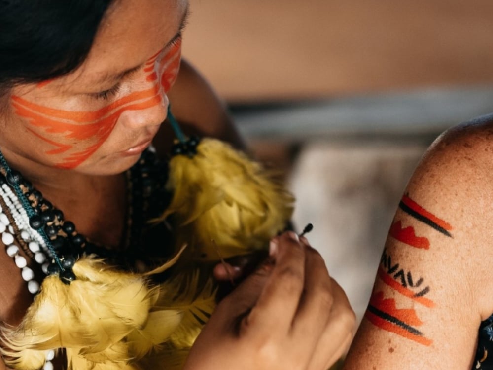 Indigenous woman applying traditional red and black face paint, representing the rich culture of local communities in the Amazon supported by ecotourism. Indigenous woman applying traditional red and black face paint, representing the rich culture of local communities in the Amazon supported by ecotourism.
