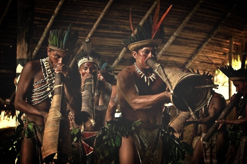 Un gruppo di indigeni dell'Amazzonia che suona lunghi strumenti a fiato tradizionali e tamburi durante un rituale culturale. Un gruppo di indigeni dell'Amazzonia che suona lunghi strumenti a fiato tradizionali e tamburi durante un rituale culturale.