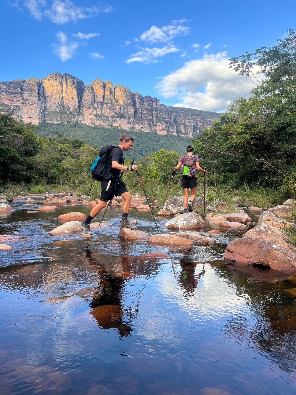 Due escursionisti attraversano un fiume con i bastoncini da trekking durante il trekking della Vale do Pati. Due escursionisti attraversano un fiume con i bastoncini da trekking durante il trekking della Vale do Pati.