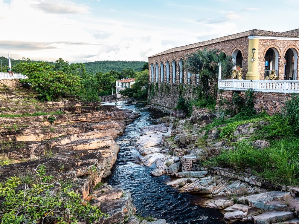 Un fiume scorre su strati di roccia accanto a un edificio coloniale con archi in pietra, nel centro storico di Igatu. Un fiume scorre su strati di roccia accanto a un edificio coloniale con archi in pietra, nel centro storico di Igatu.