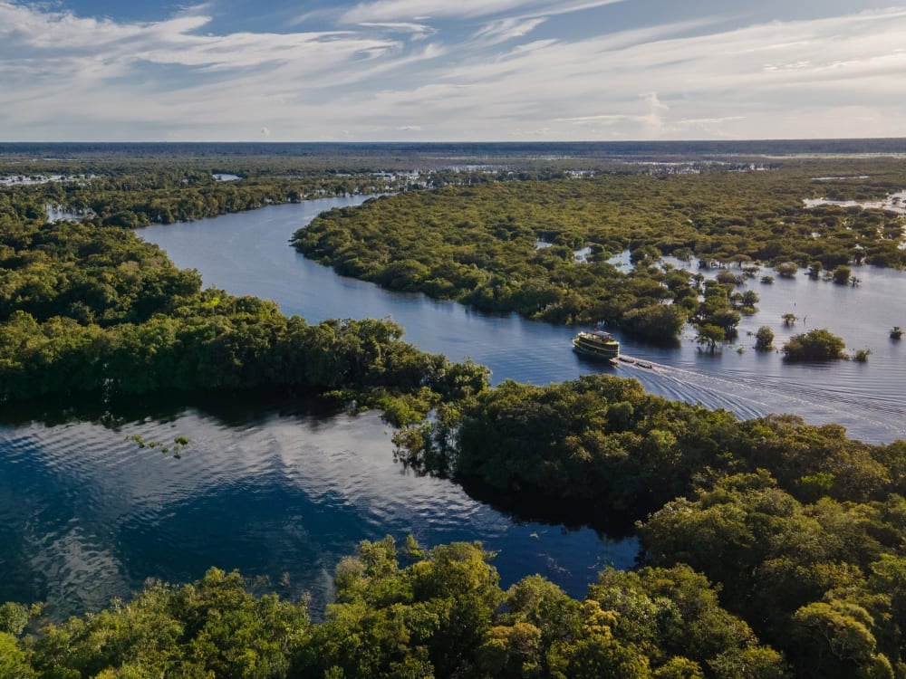 Veduta aerea di una barca Katerre che naviga tra i canali tortuosi del Rio Negro, nella foresta amazzonica, circondata da una fitta vegetazione verde. Veduta aerea di una barca Katerre che naviga tra i canali tortuosi del Rio Negro, nella foresta amazzonica, circondata da una fitta vegetazione verde.