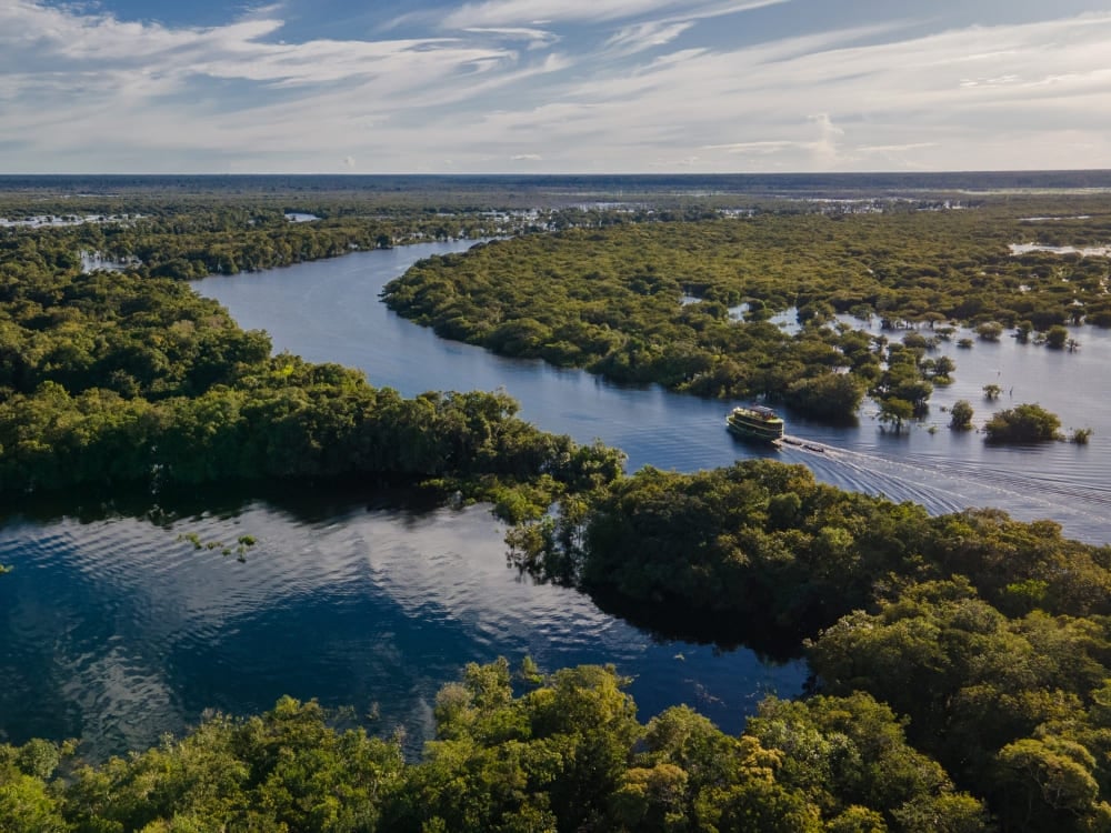 Un battello naviga in un canale tortuoso della Foresta Amazzonica circondato da una fitta volta tropicale. Un battello naviga in un canale tortuoso della Foresta Amazzonica circondato da una fitta volta tropicale.