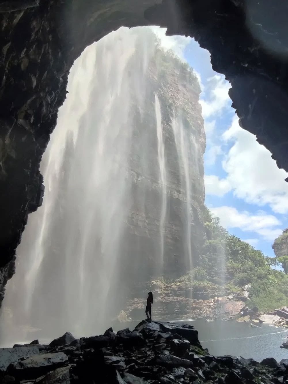 La sagoma di un escursionista in piedi sulle rocce ai piedi dell'imponente cascata do Buracão, che scorre dentro un canyon. La sagoma di un escursionista in piedi sulle rocce ai piedi dell'imponente cascata do Buracão, che scorre dentro un canyon.
