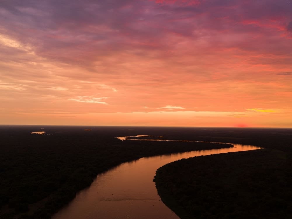 Veduta aerea di un fiume che serpeggia tra le vaste zone umide e riflette il cielo rosa e arancione della sera. Veduta aerea di un fiume che serpeggia tra le vaste zone umide e riflette il cielo rosa e arancione della sera.