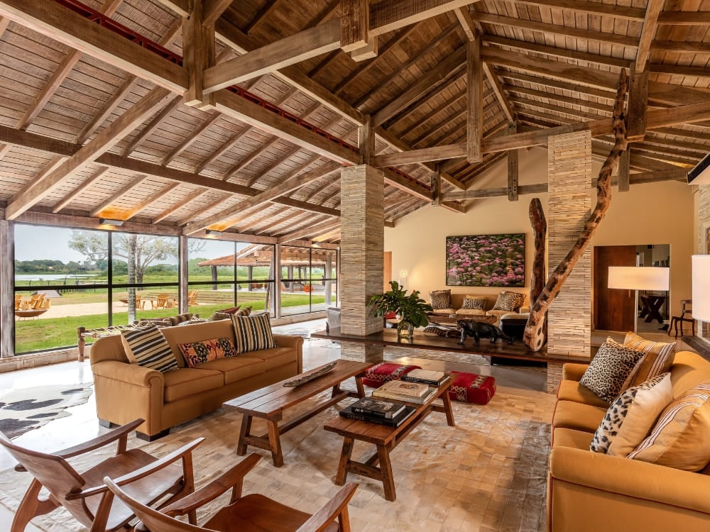 Luxurious living room with sofas, rustic wooden ceiling, and glass walls overlooking the field. Luxurious living room with sofas, rustic wooden ceiling, and glass walls overlooking the field.