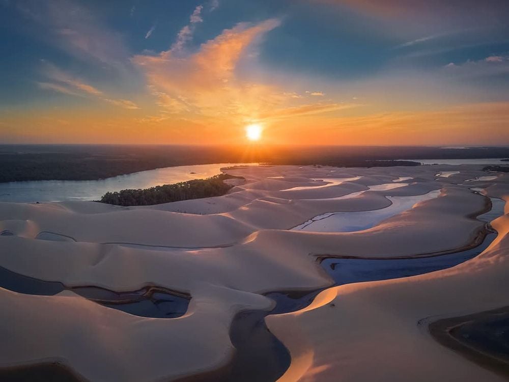 Aerial view of the dunes of Brazil with winding water channels reflecting the golden light of a vibrant sunset. Aerial view of the dunes of Brazil with winding water channels reflecting the golden light of a vibrant sunset.