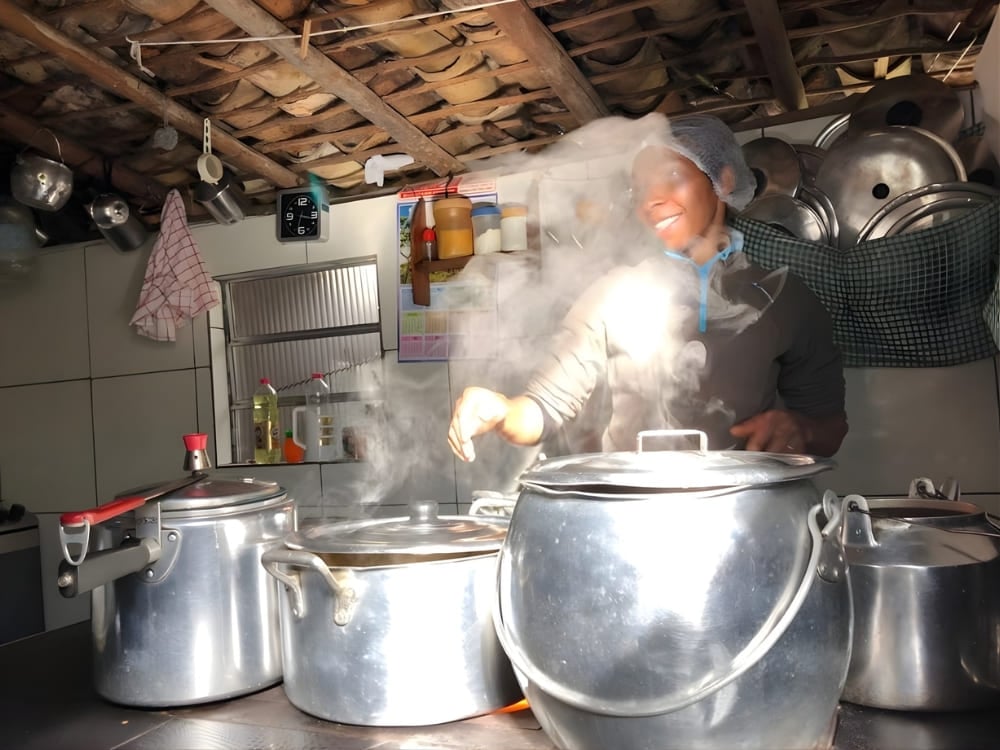 Gastvrouw kookt met grote potten in een dampende rustieke keuken, wat de nalatenschap benadrukt van inheemse vrouwen die de deuren van hun huis openzetten. Gastvrouw kookt met grote potten in een dampende rustieke keuken, wat de nalatenschap benadrukt van inheemse vrouwen die de deuren van hun huis openzetten.