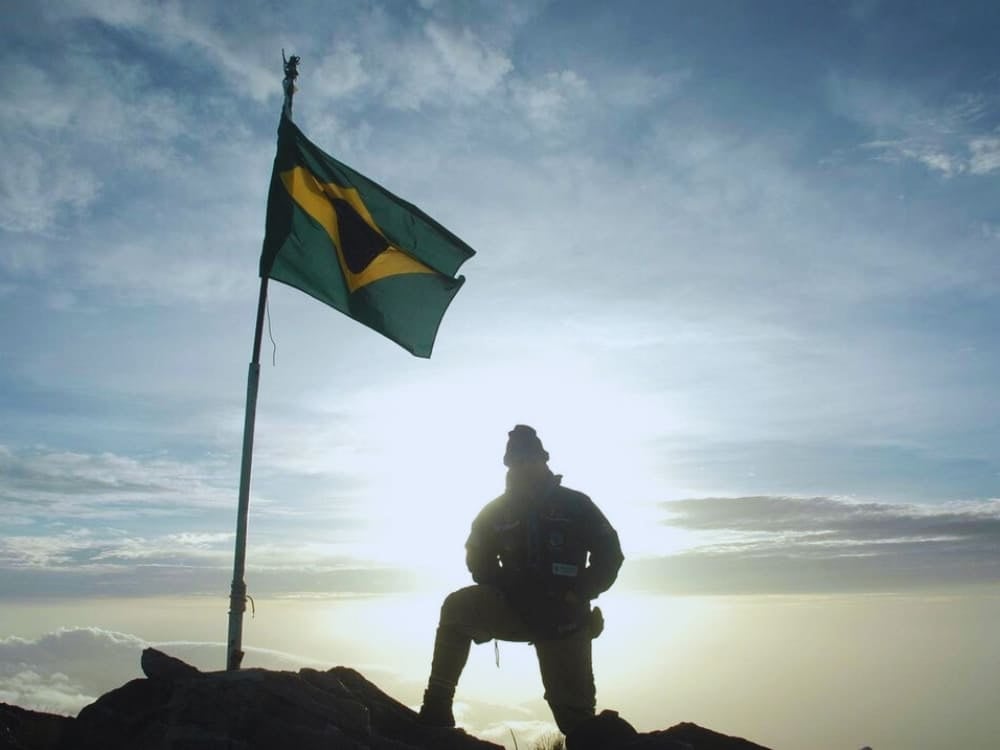 La sagoma di un esploratore inginocchiato accanto a una bandiera brasiliana che sventola sulla cima del Pico da Neblina all'alba. La sagoma di un esploratore inginocchiato accanto a una bandiera brasiliana che sventola sulla cima del Pico da Neblina all'alba.