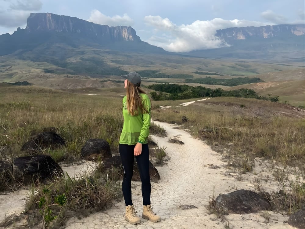 Un'ecologa in piedi su un sentiero sabbioso guarda verso la montagna tabulare del Monte Roraima in lontananza. Un'ecologa in piedi su un sentiero sabbioso guarda verso la montagna tabulare del Monte Roraima in lontananza.
