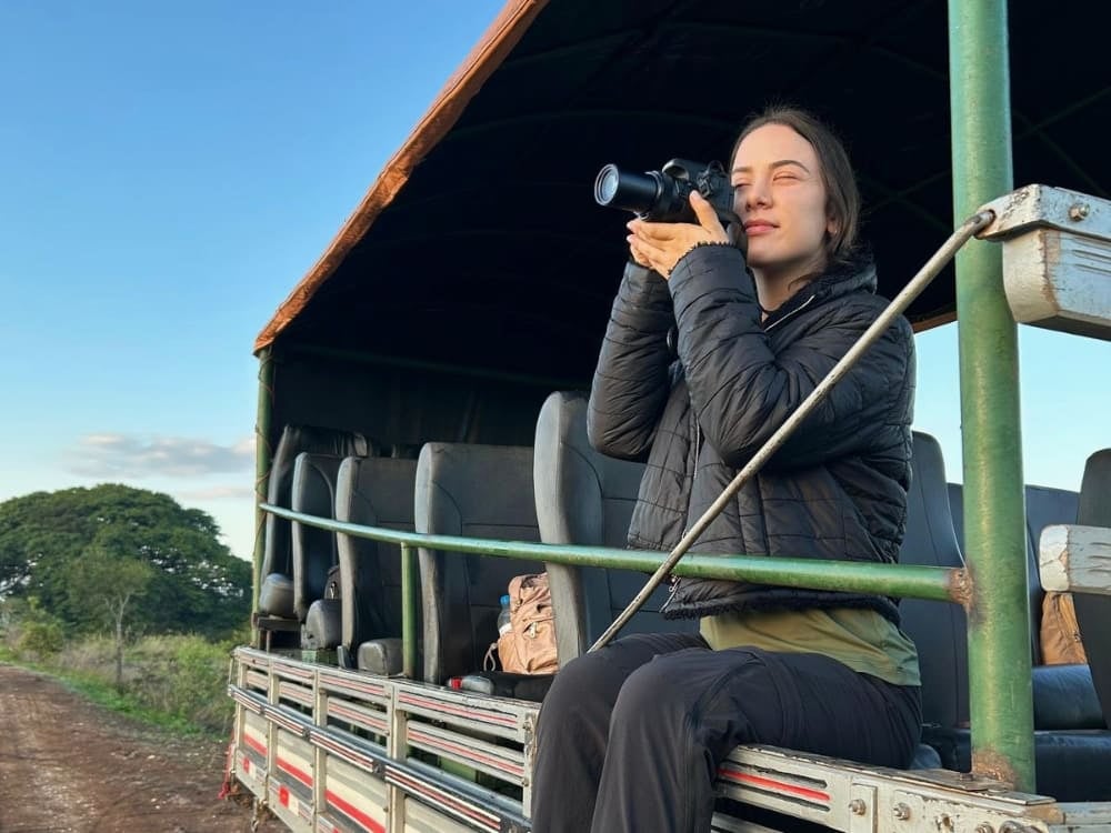 Donna che fotografa la natura dal retro di un veicolo da safari, a illustrare il lavoro di guide e fotografi naturalisti nell'ecoturismo. Donna che fotografa la natura dal retro di un veicolo da safari, a illustrare il lavoro di guide e fotografi naturalisti nell'ecoturismo.