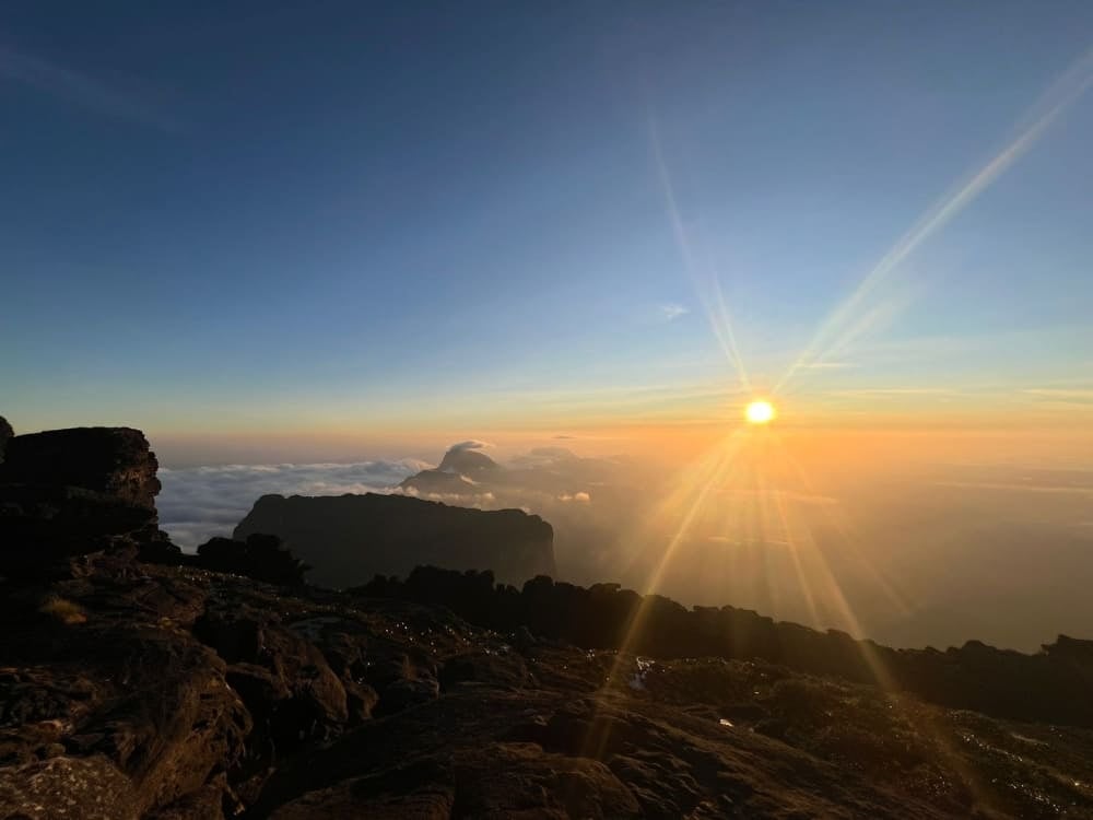 Il sole esplode con raggi luminosi sopra un mare di nuvole bianche e montagne tabulari in controluce, visto dalla cima rocciosa del Monte Roraima. Il sole esplode con raggi luminosi sopra un mare di nuvole bianche e montagne tabulari in controluce, visto dalla cima rocciosa del Monte Roraima.