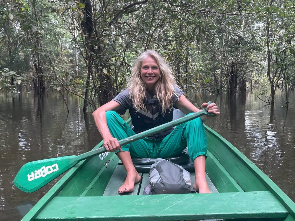 Katharina, bionda e sorridente, con la pagaia in mano mentre naviga su una canoa verde in una foresta allagata dell'Amazzonia. Katharina, bionda e sorridente, con la pagaia in mano mentre naviga su una canoa verde in una foresta allagata dell'Amazzonia.