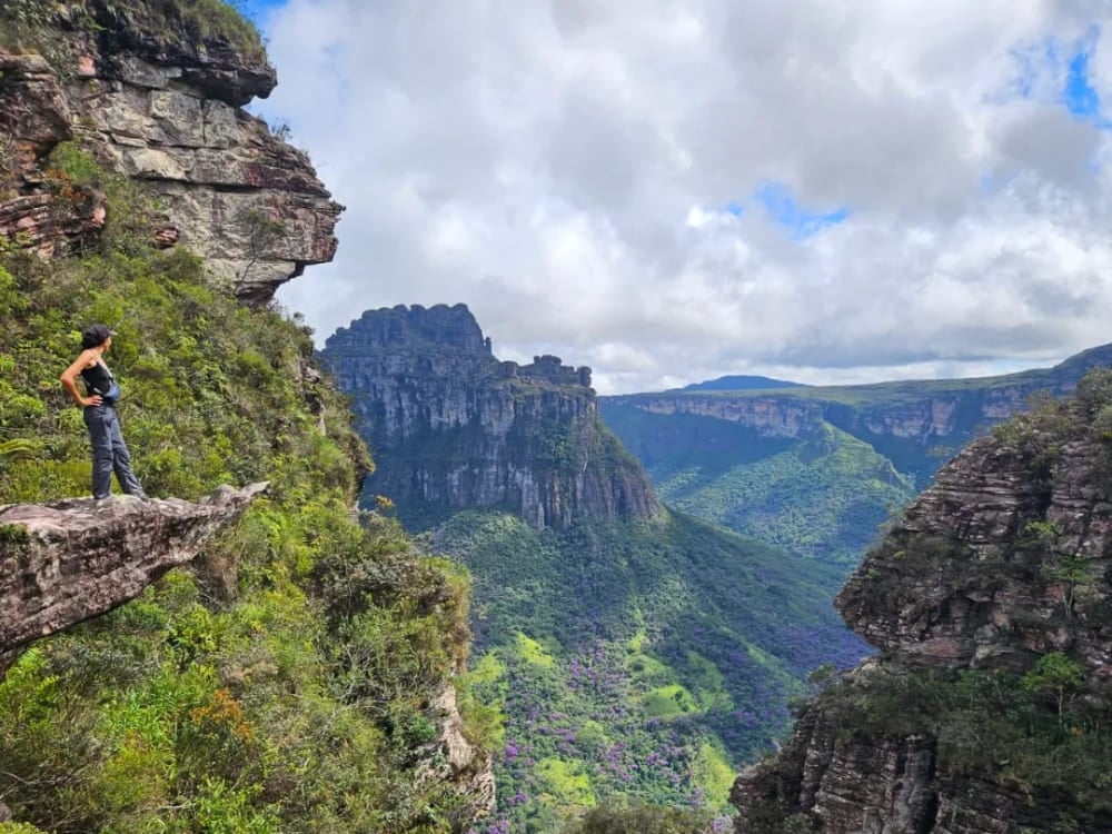 Donna in piedi sul bordo di uno sperone di roccia che ammira montagne e valli, a simboleggiare le esperienze autentiche guidate dalle donne nell'ecoturismo. Donna in piedi sul bordo di uno sperone di roccia che ammira montagne e valli, a simboleggiare le esperienze autentiche guidate dalle donne nell'ecoturismo.