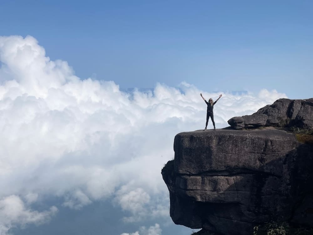 Silhouette di una donna con le braccia alzate in segno di vittoria sul bordo della parete rocciosa del Monte Roraima, sopra le nuvole bianche. Silhouette di una donna con le braccia alzate in segno di vittoria sul bordo della parete rocciosa del Monte Roraima, sopra le nuvole bianche.