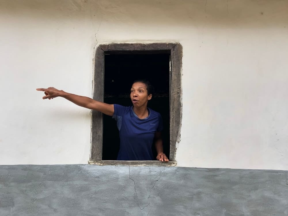 Donna con una camicetta azzurra che indica qualcosa oltre la finestra di una casa rustica, a rappresentare la forza femminile in prima linea nei viaggi di natura in Brasile. Donna con una camicetta azzurra che indica qualcosa oltre la finestra di una casa rustica, a rappresentare la forza femminile in prima linea nei viaggi di natura in Brasile.