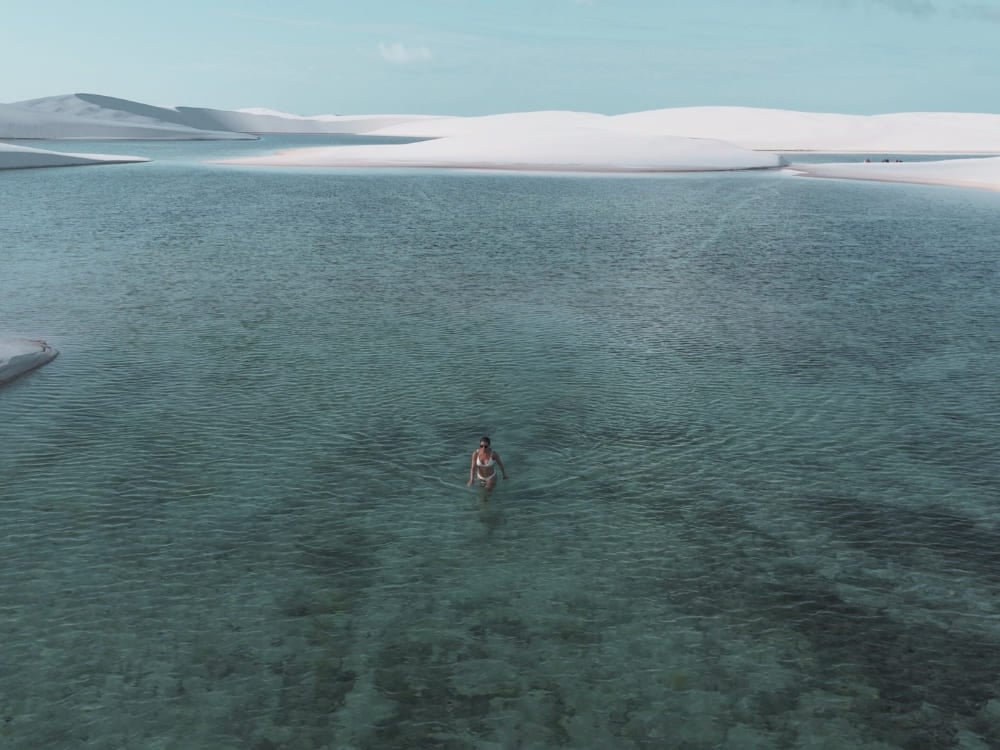 Donna che cammina nelle acque basse e cristalline di una laguna circondata dalle grandi dune di sabbia bianca dei Lençóis Maranhenses. Donna che cammina nelle acque basse e cristalline di una laguna circondata dalle grandi dune di sabbia bianca dei Lençóis Maranhenses.