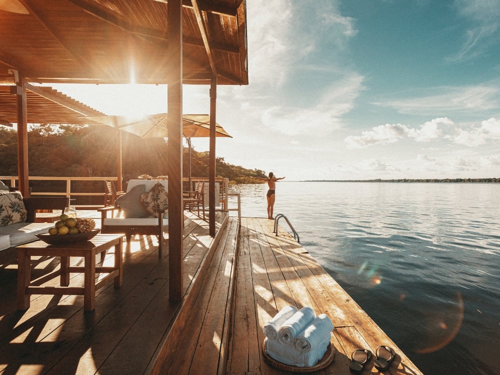 Person with open arms on the floating wooden deck of an Amazon ecolodge at sunset. Person with open arms on the floating wooden deck of an Amazon ecolodge at sunset.
