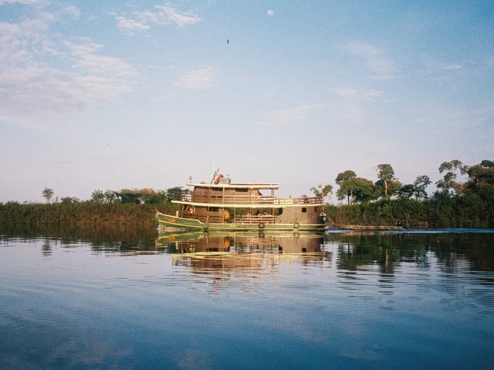 Tradizionale barca da crociera fluviale che naviga sulle acque calme del Rio Negro, con la vegetazione verde che si riflette sull'acqua. Tradizionale barca da crociera fluviale che naviga sulle acque calme del Rio Negro, con la vegetazione verde che si riflette sull'acqua.