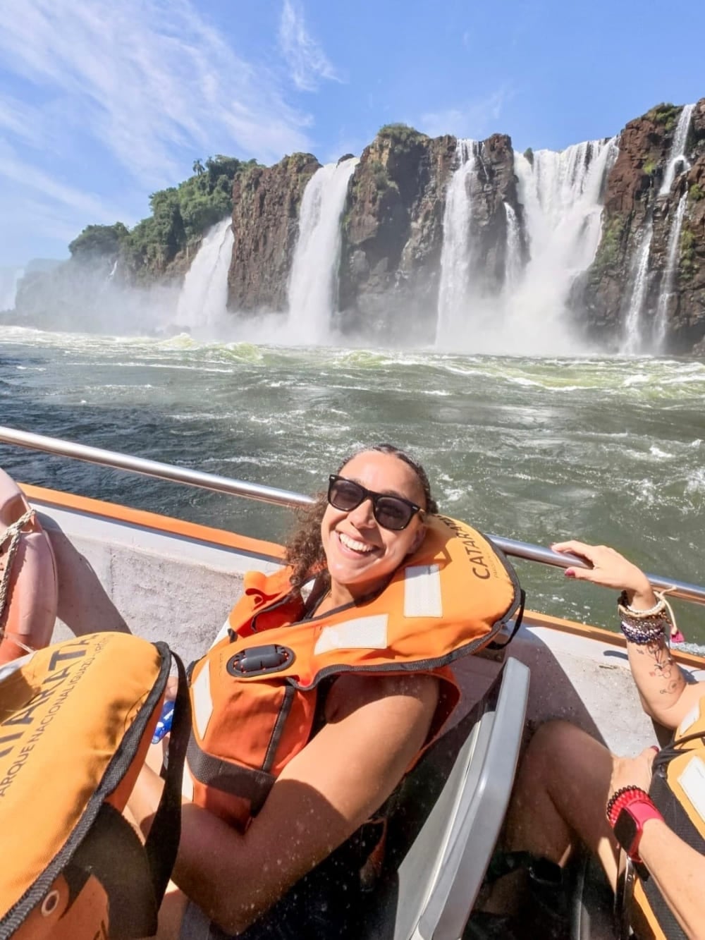 Samantha Sage, con occhiali da sole e giubbotto di salvataggio arancione, sorride durante un'escursione in barca vicino a enormi cascate, in Brasile. Samantha Sage, con occhiali da sole e giubbotto di salvataggio arancione, sorride durante un'escursione in barca vicino a enormi cascate, in Brasile.