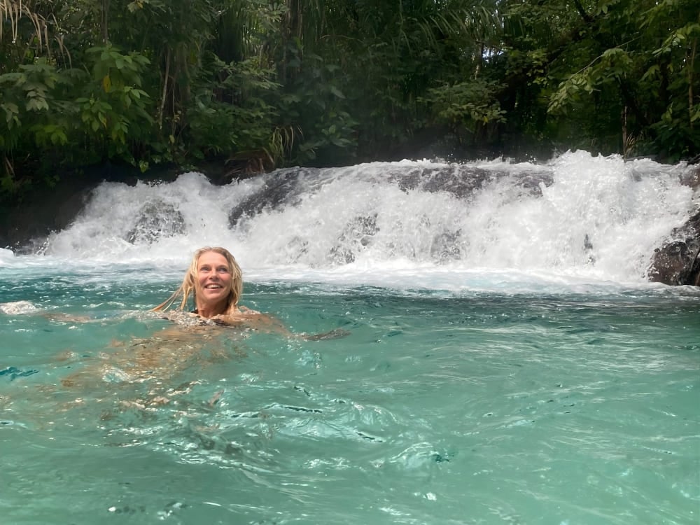 Donna sorridente che nuota in acque azzurre e cristalline con una grande cascata sullo sfondo, nella regione del Jalapão. Donna sorridente che nuota in acque azzurre e cristalline con una grande cascata sullo sfondo, nella regione del Jalapão.
