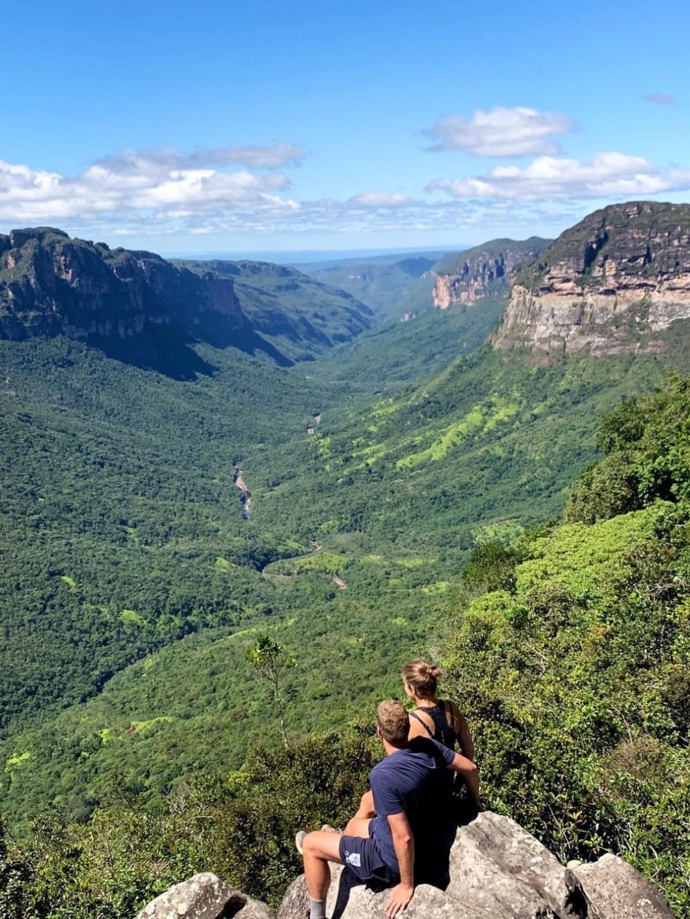 Twee wandelaars zitten op een rotsachtige klif en bewonderen de uitgestrekte, groene vlakte van Vale do Pati in Nationaal Park Chapada Diamantina. Twee wandelaars zitten op een rotsachtige klif en bewonderen de uitgestrekte, groene vlakte van Vale do Pati in Nationaal Park Chapada Diamantina.