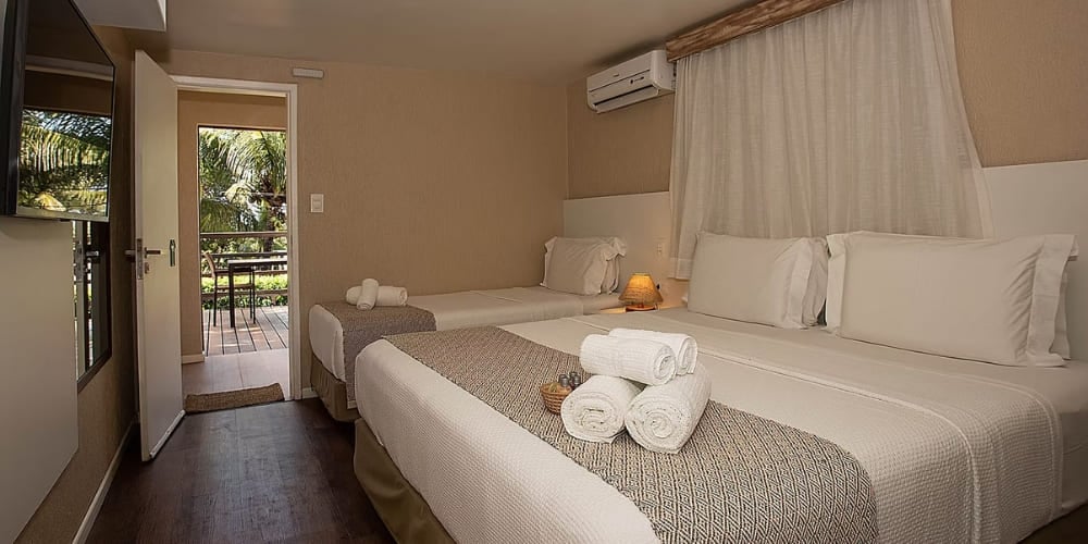 Camera accogliente con un letto matrimoniale, un letto singolo e una porta aperta che dà su un balcone soleggiato, in una struttura di Fernando de Noronha. Camera accogliente con un letto matrimoniale, un letto singolo e una porta aperta che dà su un balcone soleggiato, in una struttura di Fernando de Noronha.