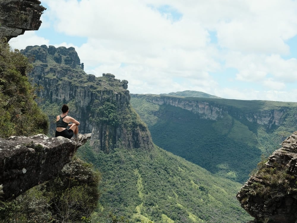 Een backpacker zit op een grillige rotsrand en geniet van een panoramisch uitzicht op de steile kliffen en ongerepte groene valleien van Vale do Pati. Een backpacker zit op een grillige rotsrand en geniet van een panoramisch uitzicht op de steile kliffen en ongerepte groene valleien van Vale do Pati.
