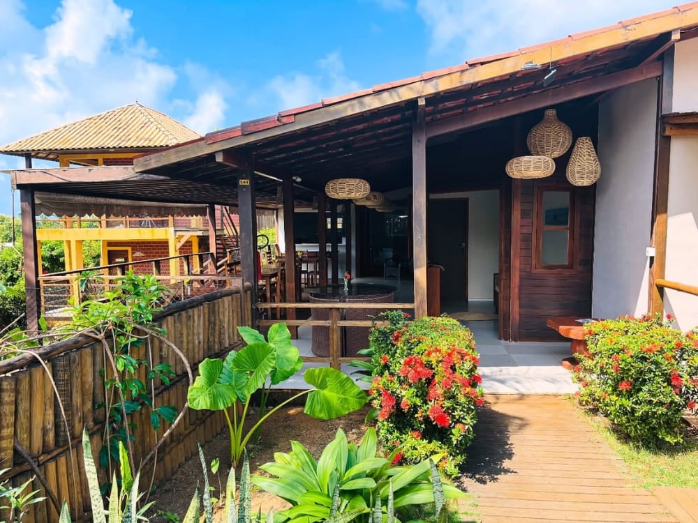 Esterno di una guest house con portico coperto, pilastri in legno e giardino tropicale verde a Fernando de Noronha. Esterno di una guest house con portico coperto, pilastri in legno e giardino tropicale verde a Fernando de Noronha.