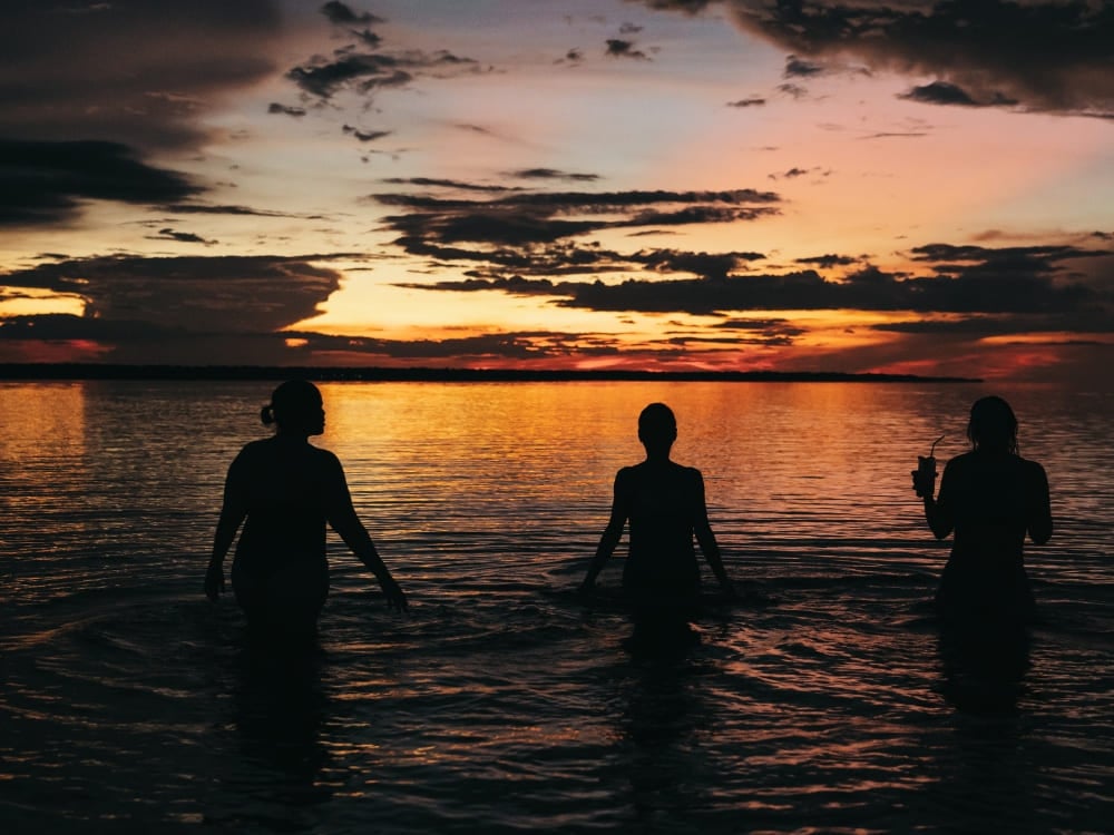 Siluetas de tres personas de pie con el agua por la cintura en el Amazonas al atardecer. Siluetas de tres personas de pie con el agua por la cintura en el Amazonas al atardecer.