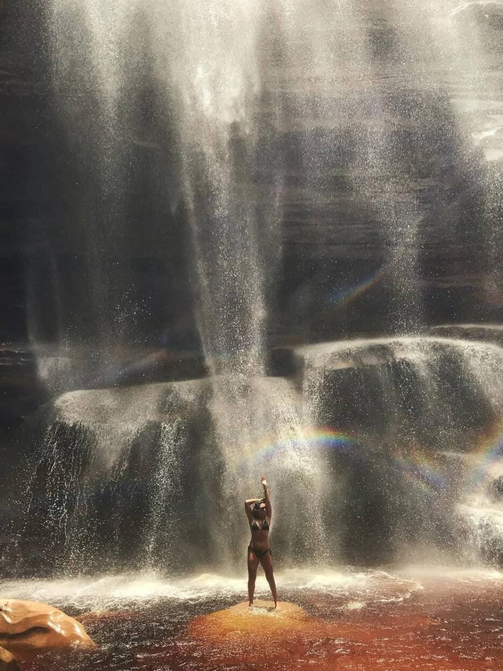 Una donna in piedi su una roccia allarga le braccia alla base della cascata do Mosquito, alta 60 metri, dentro un'ampia piscina naturale. Una donna in piedi su una roccia allarga le braccia alla base della cascata do Mosquito, alta 60 metri, dentro un'ampia piscina naturale.