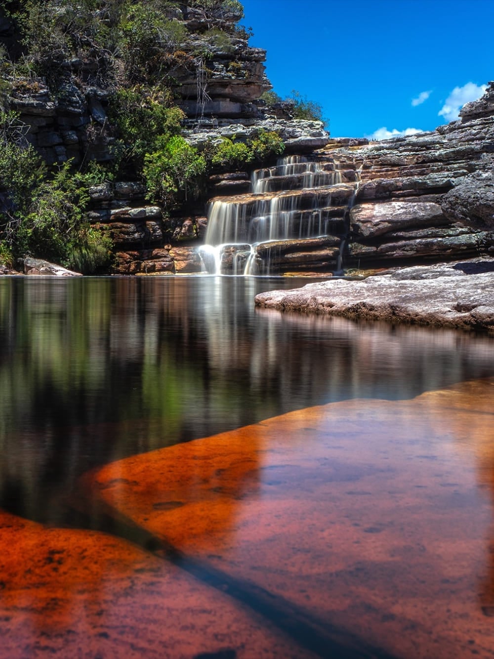 Una cascata scende in una piscina naturale calma tra rocce rosse, nel Parco Nazionale Chapada Diamantina. Una cascata scende in una piscina naturale calma tra rocce rosse, nel Parco Nazionale Chapada Diamantina.