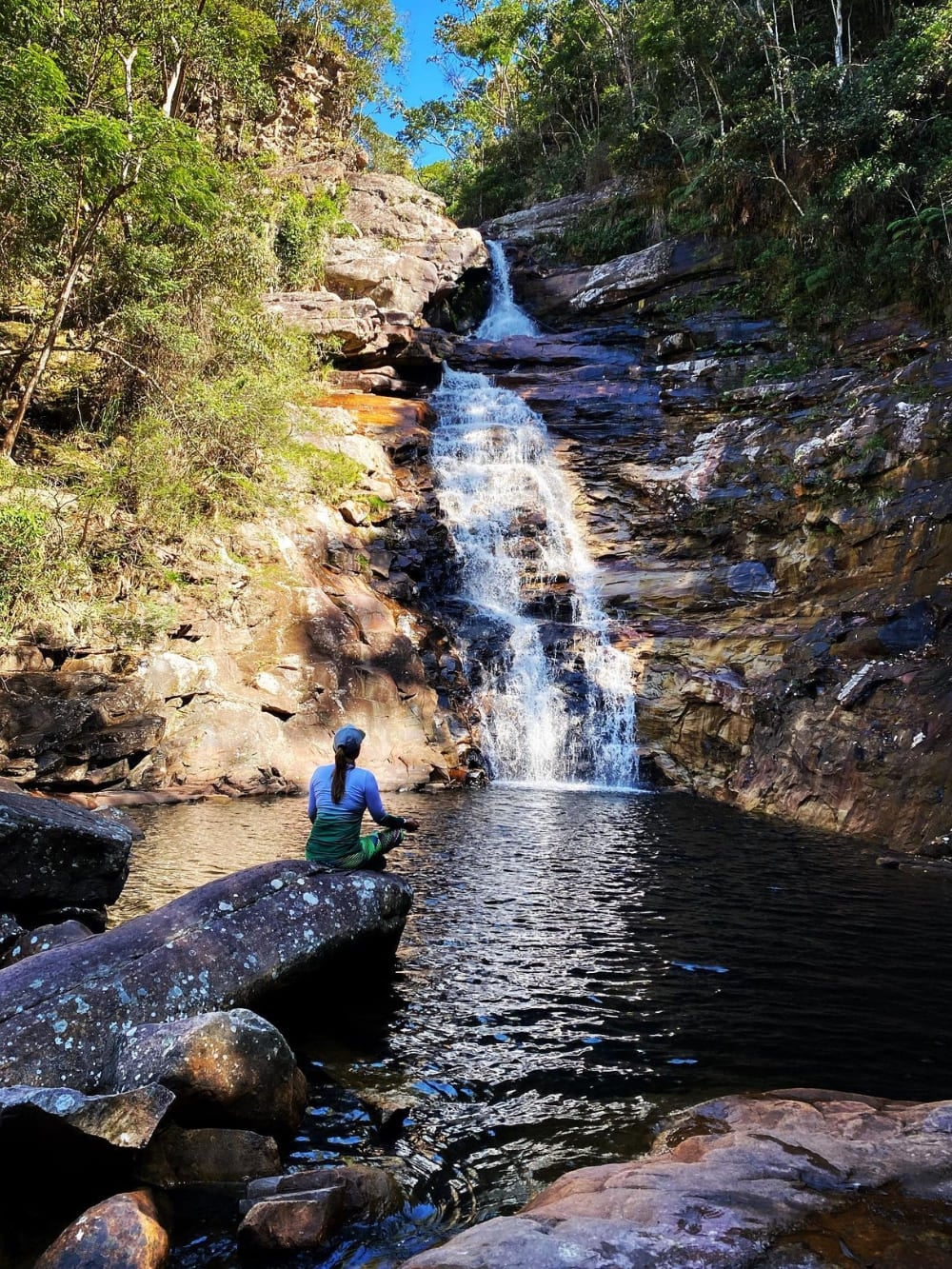 Una donna seduta su una roccia accanto alla piscina naturale calma della cascata do Funil, un salto di 20 metri circondato da vegetazione fitta. Una donna seduta su una roccia accanto alla piscina naturale calma della cascata do Funil, un salto di 20 metri circondato da vegetazione fitta.